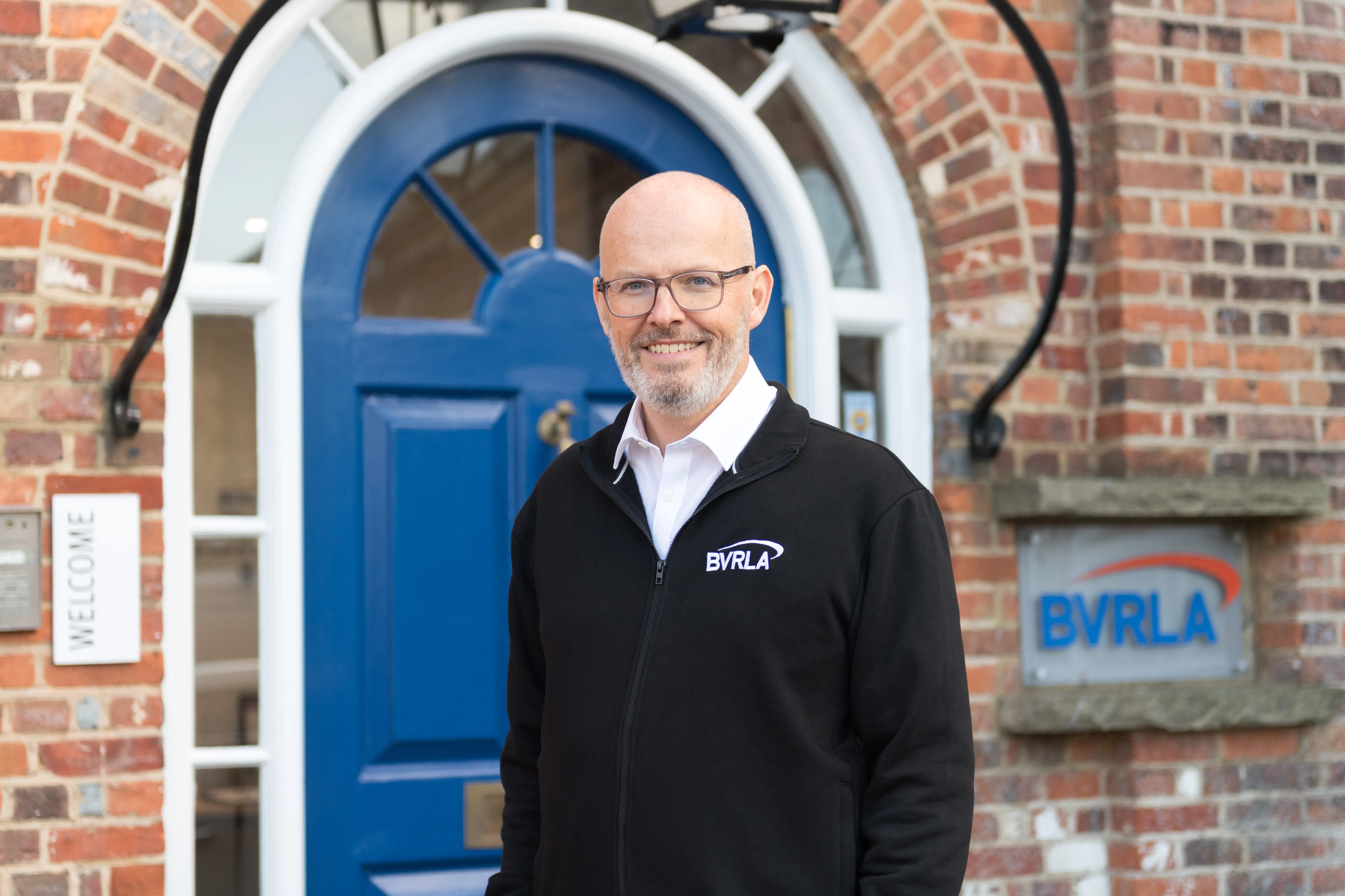 BVRLA Chief Executive Toby Poston stood in front of the brick building and blue front door.