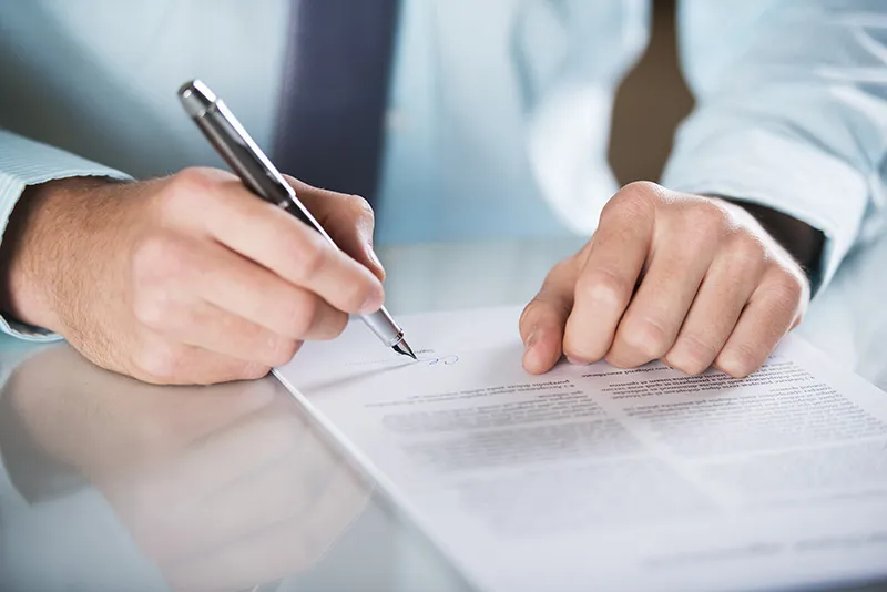 A man in a shirt with a pen is signing an official document