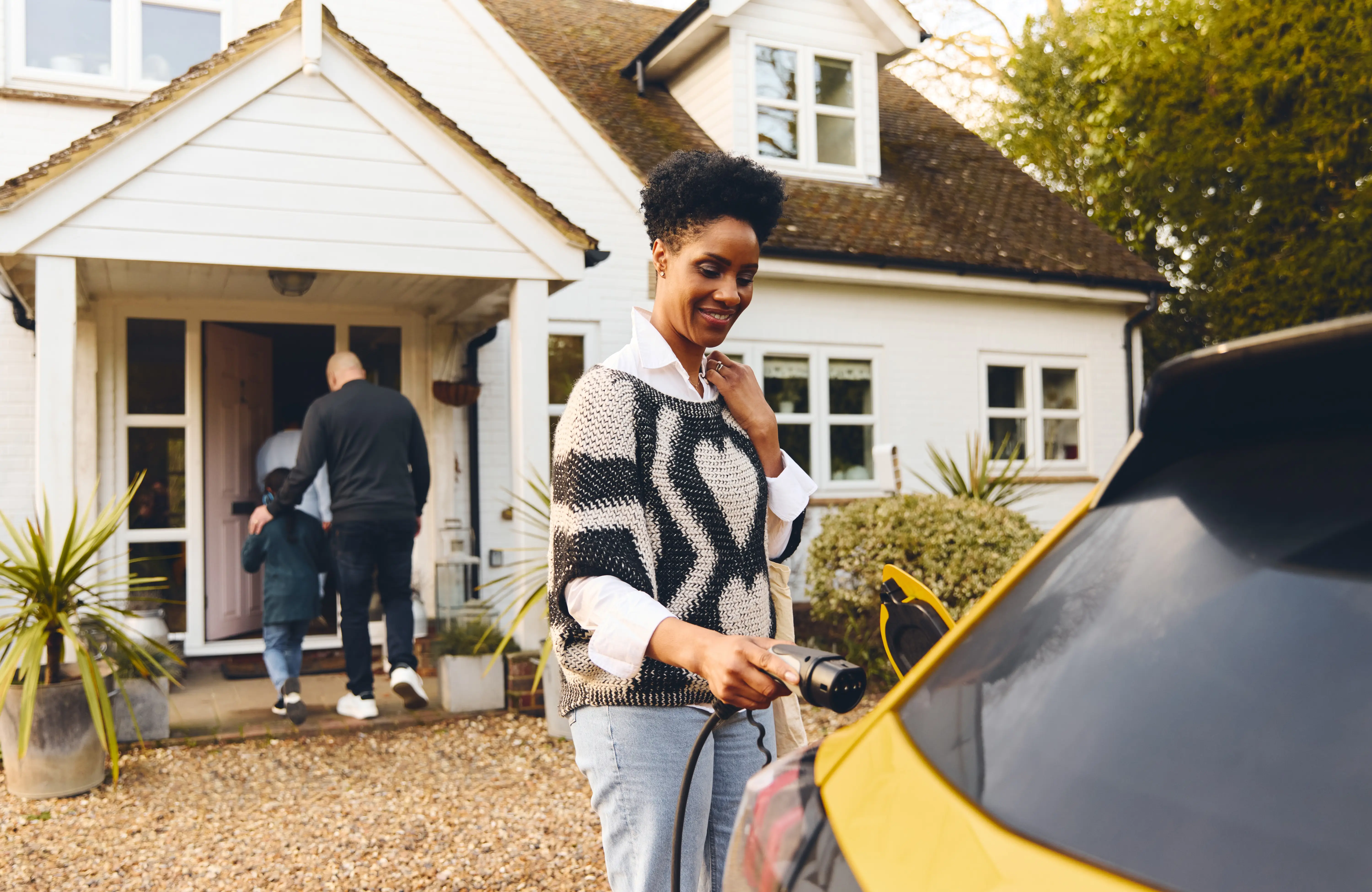 Woman plugging in electric charger into car with family outside home
