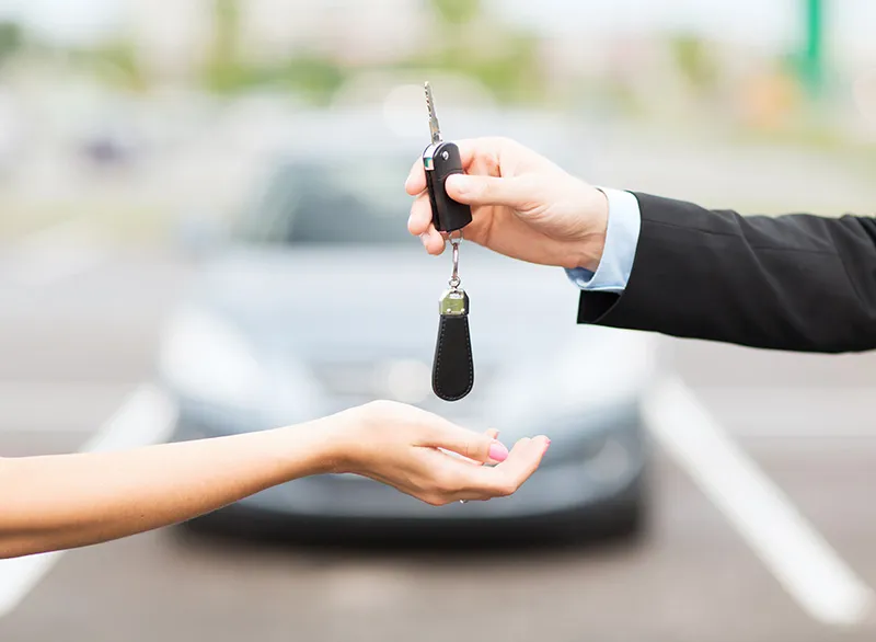 Man is placing a car key in woman's hand, there's a blurred car in background