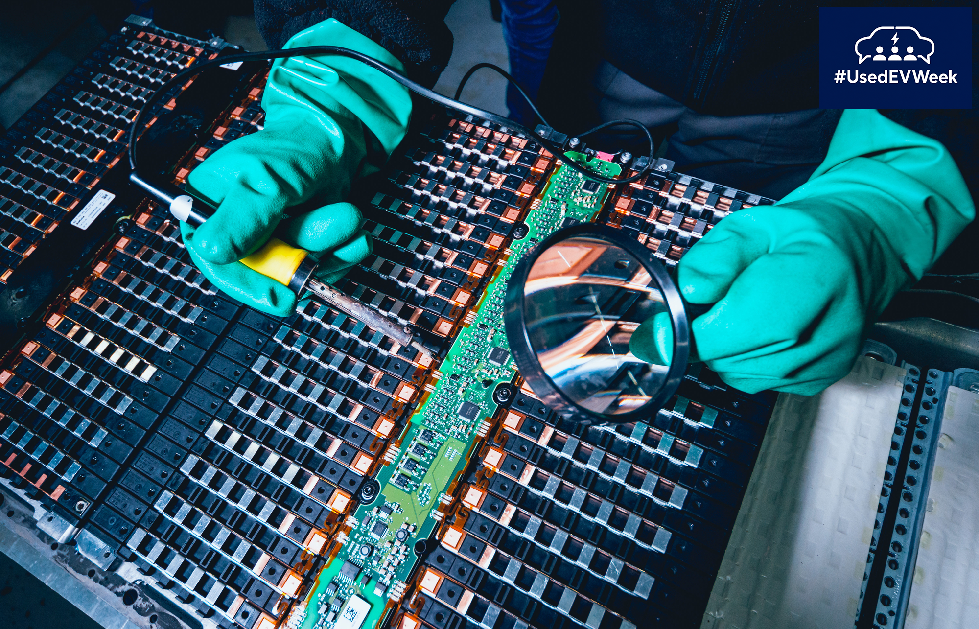 An EV battery being assessed by a technician in bright turquoise gloves, with Used EV Week logo