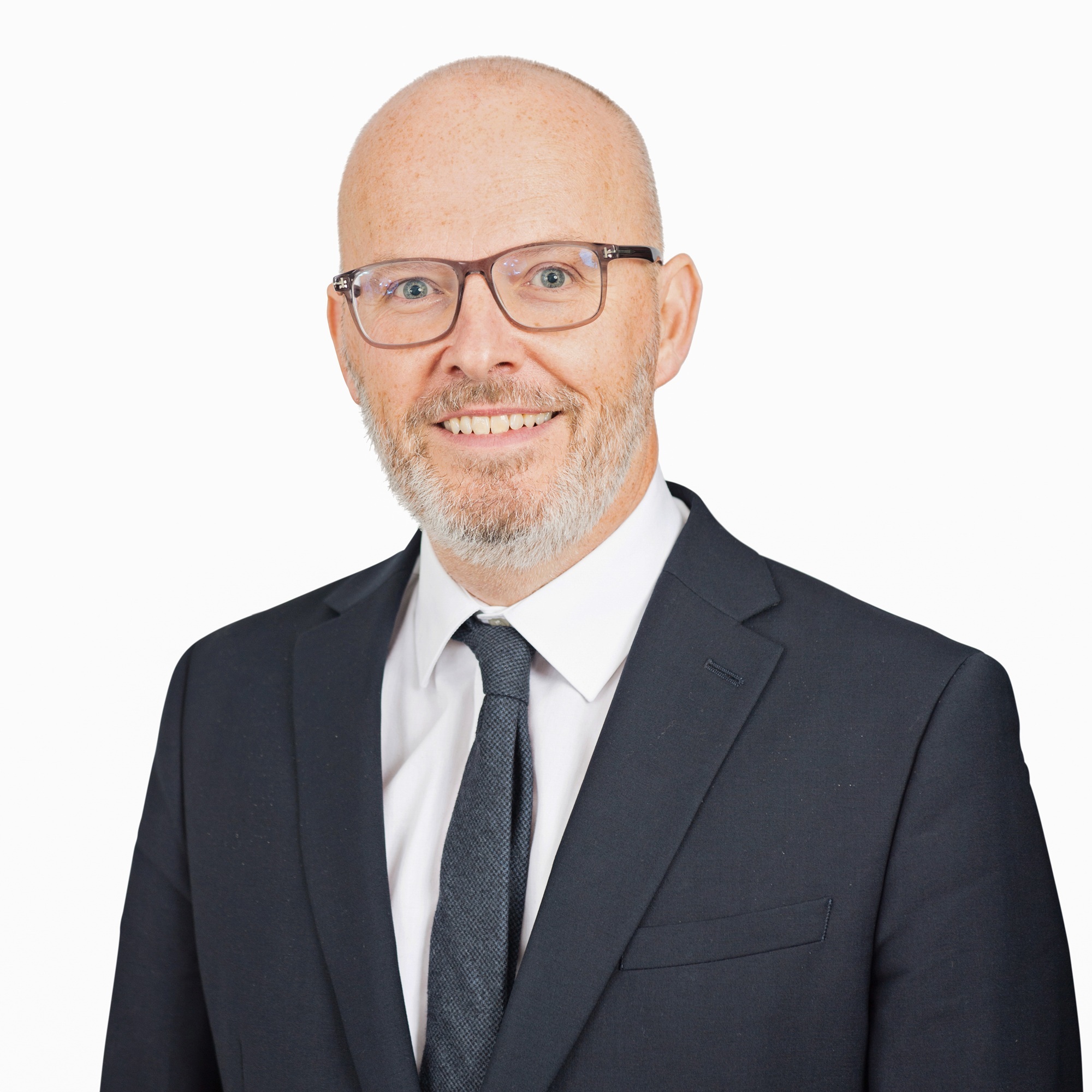 Headshot of Toby Poston on a white background. Toby is wearing glasses, a smart white shirt and dark suit jacket