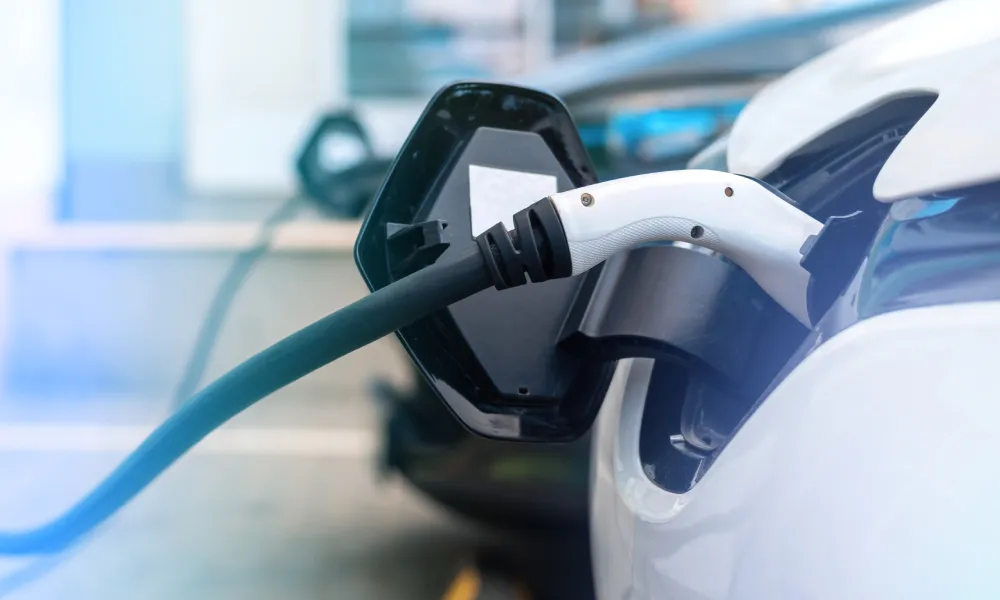 Two electric cars charging, with a white car in the foreground and a darker car behind