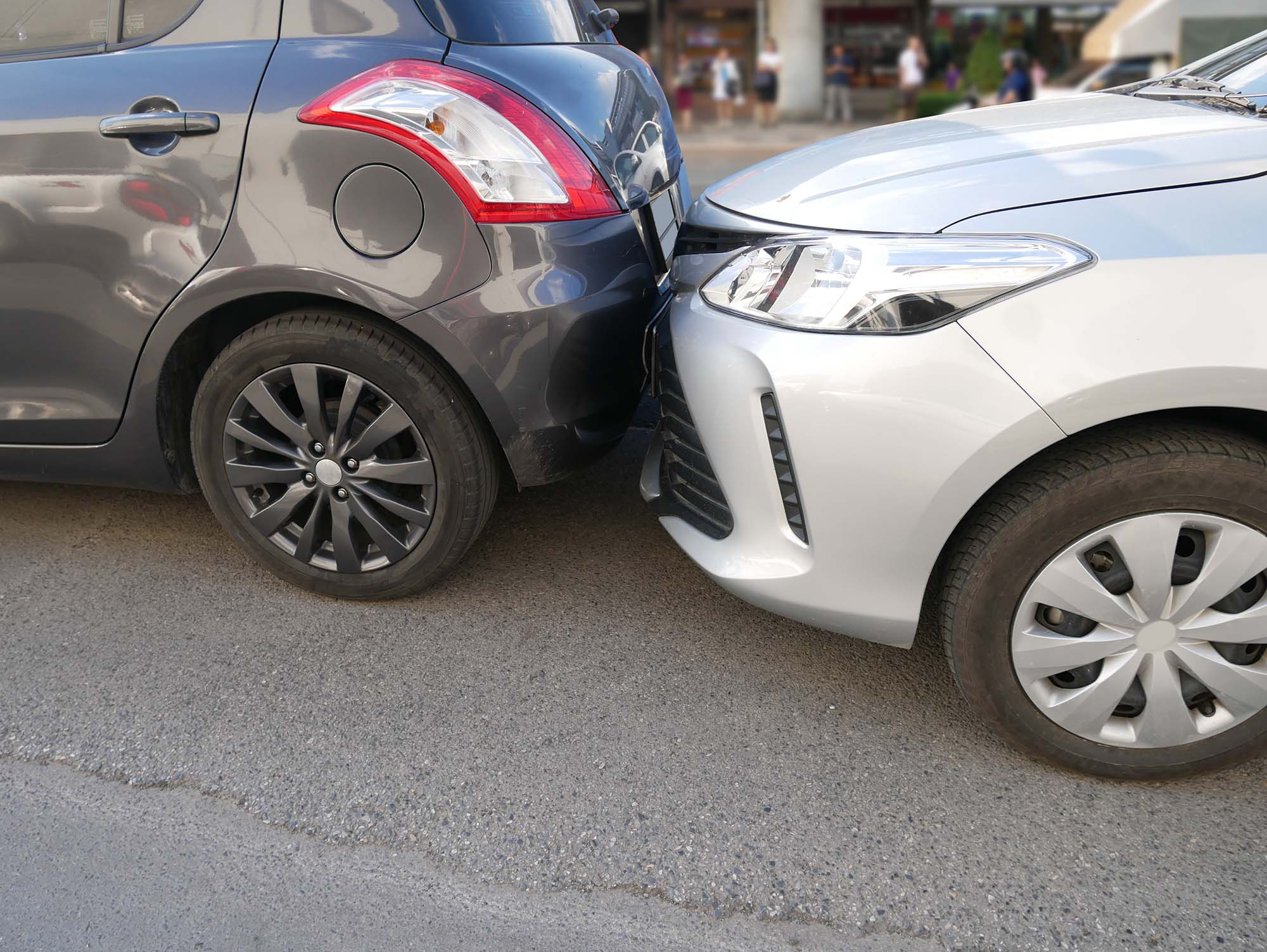 A dark grey car and a light grey car shown involved in an accident where one car hits other up the rear